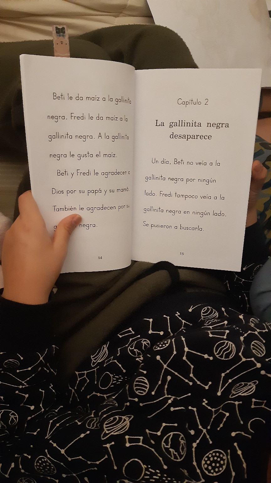 Un niño sostiene un libro abierto mientras lee en la cama, sin mostrar su rostro