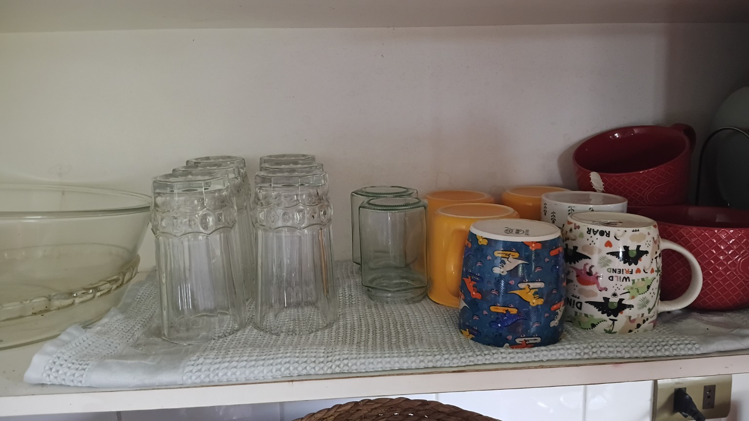 Vasos y tazas organizados sobre un paño en el estante del mueble
